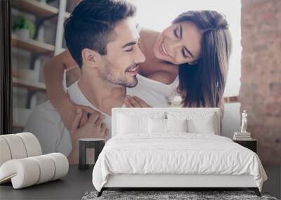 Beautiful couple of young lovers are hugging indoors at home, looking at each other with love and tenderness, wearing white casual clothes Wall mural