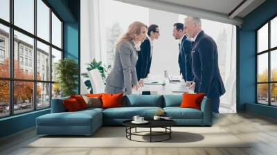 Business competition, four stylish business persons in suits having disagreement and conflict, standing together near desktop in front of each other, face to face with disrespect expression Wall mural