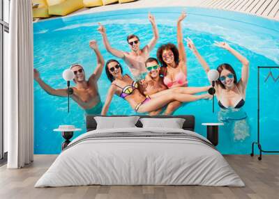 Chilling, dancing international youth, enjoying on resort beach pool sunny disco in the water, in diverse trendy fashionable bikinies, spectacles, celebrating holiday, guy holds two ladies on hands Wall mural