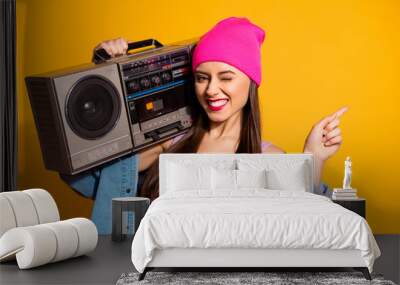 Close up photo funny she her lady hold vintage audio recorder shoulder indicate finger empty space advising buy buyer novelty wear casual jeans denim jacket pink hat isolated yellow vivid background Wall mural