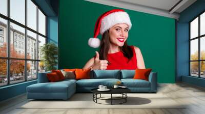 Close-up portrait of her she nice attractive charming pretty lovely glad cheerful cheery girl wearing Santa cap showing thumbup advice advert ad Eve Noel isolated over green color background Wall mural