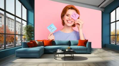 Close-up portrait of her she nice cute charming attractive cheerful girl wearing casual blue t-shirt holding in hands two draw notes positive good choice isolated on pink pastel background Wall mural