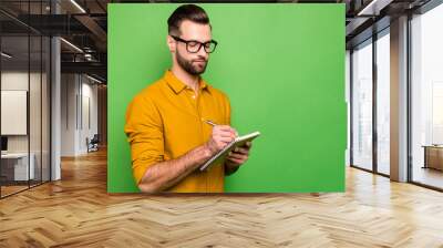 Close-up portrait of his he nice attractive focused intelligent bearded guy in casual formal shirt office manager writing schedule isolated on bright vivid shine vibrant green color background Wall mural