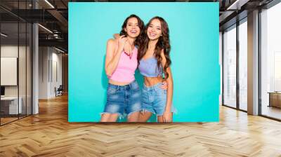 Close up portrait two stunning beautiful friendly she her lady chic hugging revealing white teeth toothy wearing pink jeans denim shorts tank tops isolated blue teal bright vivid background Wall mural