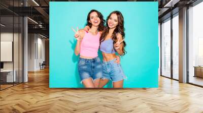 Close up portrait two stunning beautiful she her lady chic hugging white teeth toothy show v-sign wearing shiny jeans denim shorts tank tops isolated green teal bright vivid background Wall mural