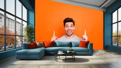 Closeup photo of attractive funny guy hold hands fingers direct up empty space excited good mood sales person nice offer wear striped t-shirt isolated bright orange color background Wall mural