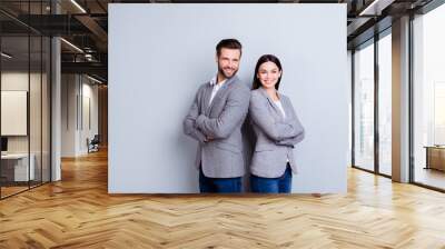 Concept of partnership in business. Young man and woman standing back-to-back with crossed hands against gray background Wall mural