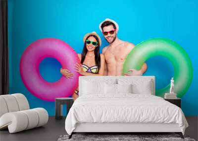 Concept of summer vacation and honeymoon. Guy and girl dressed in beachwear hold inflatable life ring standing isolated on blue background Wall mural