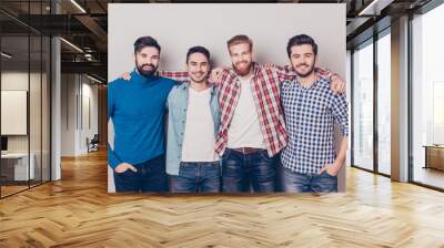 Diversity of men. Four cheerful young guys are standing and embracing, smiling, on pure background in casual outfit and jeans Wall mural