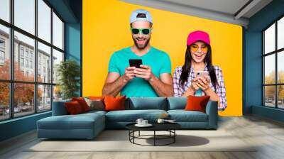 Electronic wireless device sms media cellular concept. Portrait of joyful cheerful couple using smart phones typing message browsing 3G wifi internet isolated on vivid yellow background Wall mural