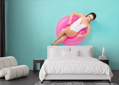 Full body high angle above view photo of gentle lady bronze skin sitting swimming pool big life buoy flirty eyes wear white swim bodysuit isolated pastel teal color background Wall mural