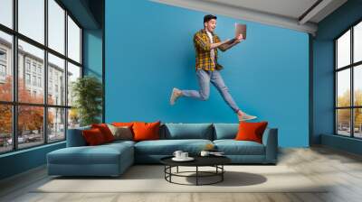 Full body length photo addicted programmer loves doing his job in deadline running jumping with computer isolated on blue color background Wall mural