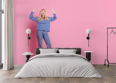 Full body photo of attractive mature woman point look up empty space dressed stylish striped clothes isolated on pink color background Wall mural