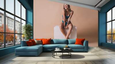 Full body photo of attractive young girl sit white cube laughing wear cyan fashion lingerie isolated beige background no filter Wall mural