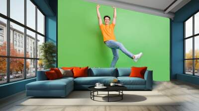 Full body photo of cheerful triumphant luck man raise hands winner hooray isolated on green color background Wall mural