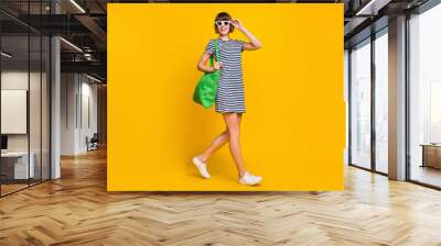 Full body photo of cute brunette millennial lady go wear dress sneakers bag eyewear isolated on yellow background Wall mural