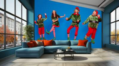 Full body photo of positive childhood elf people dance xmas wear hat holiday enjoy isolated on red color background Wall mural