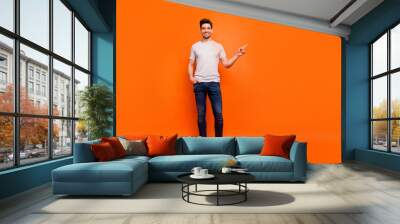 Full body photo of sales man guy cheerful person street casual look clothes directing finger empty space wear striped t-shirt jeans shoes isolated bright orange color background Wall mural