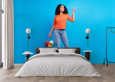 Full body photo of young afro woman happy smile point finger empty space advert suggest mall shop isolated over blue color background Wall mural