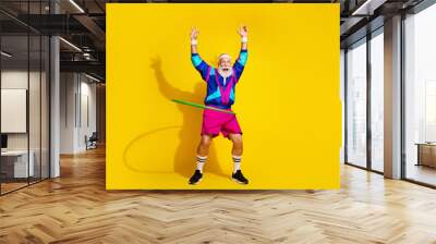 Full body portrait of eccentric aged man spinning hula hoop empty space workout retro sportswear isolated on yellow color background Wall mural