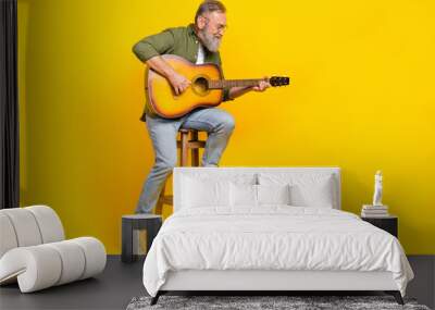 Full body portrait of positive peaceful aged man sitting chair hold play guitar isolated on yellow color background Wall mural