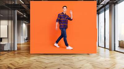 Full body profile photo of young cute guy go wave wear shirt jeans sneakers isolated on orange background Wall mural