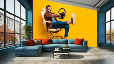 Full length body photo of happy fooling man in chair keeping steering wheel pretending car driver isolated vivid yellow color background Wall mural