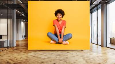 Full length body size photo of curly cheerful funny cute sweet nice pretty african woman sitting on floor with her legs crossed wearing jeans denim isolated voer bright color background Wall mural