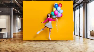 Full length body size photo of funny pretty young girl jumping up high holding air balloons smiling laughing isolated on bright yellow color background Wall mural