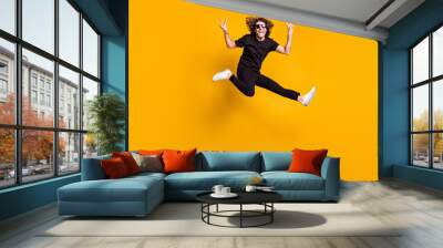 Full length body size portrait of young man jumping happily wearing black clothes demonstrating v-sign gesture with both hands isolated on bright yellow color background Wall mural