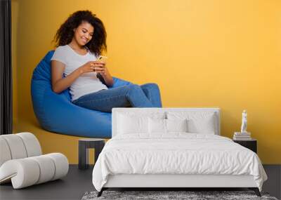 Full length body size turned photo of cheerful curly wavy brown haired positive girl browsing through her phone answering in comments of her repost isolated over vivid color background Wall mural