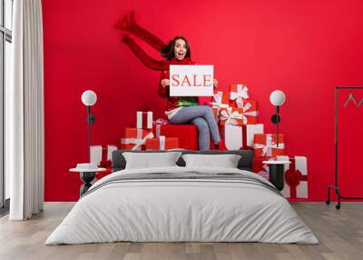 Full length body size view of her she attractive pretty cheerful cheery girl sitting on big giftbox holding in hand advert promo card isolated bright vivid shine vibrant red color background Wall mural