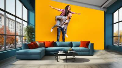 Full length body size view of lovely cheerful couple piggy backing having fun fooling copy space isolated over bright yellow color background Wall mural