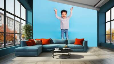 Full length body size view of nice cheerful amazed boy rising hands up isolated over bright blue color background Wall mural