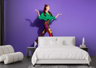 Full length photo cute girl wear print trousers shirt flying look empty space palms hold objects isolated on violet color background Wall mural