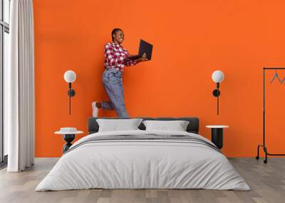 Full length photo of carefree excited person jump write email wireless netbook isolated on orange color background Wall mural