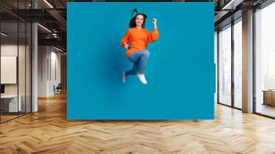 Full length photo of charming positive girl wear orange sweater jumping high running empty space isolated blue color background Wall mural