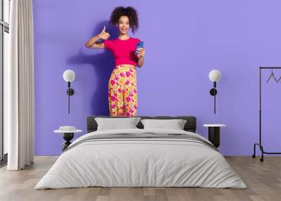 Full length photo of charming positive woman wear pink top showing thumb up chatting modern gadget empty space isolated violet color background Wall mural