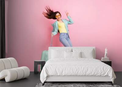 Full length photo of cheerful crazy young woman show v-sign trip hold baggage isolated on pastel pink color background Wall mural