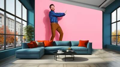 Full length photo of cheerful funny man wear stylish clothes push heavy empty space isolated on pink color background Wall mural