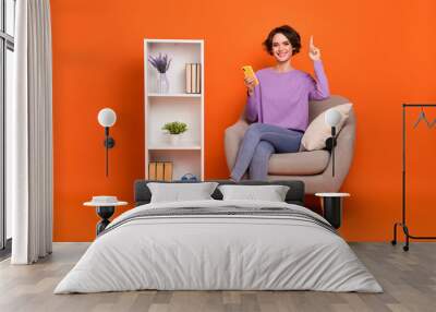 Full length photo of cheerful girl sit chair point finger purchase house interior isolated on orange color background Wall mural