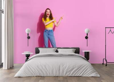 Full length photo of cheerful pretty lady dressed yellow t-shirt pointing two fingers empty space isolated pink color background Wall mural