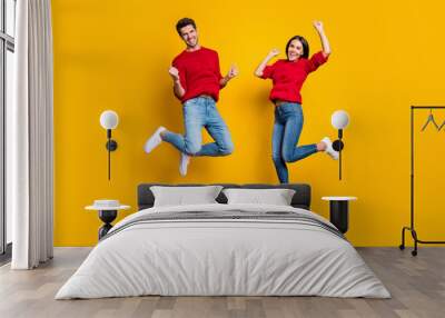 Full length photo of cheerful woman and man jump raise fists scream yes celebrate victory wear red sweater denim jeans isolated over yellow background Wall mural