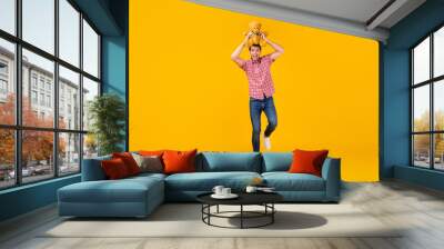 Full length photo of cheerful young man hold bear toy above head walk isolated on yellow color background Wall mural