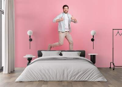 Full length photo of cool confident guy dressed teal shirt jumping high thumbs up isolated pink color background Wall mural