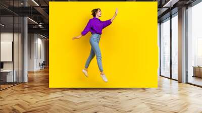 Full length photo of dreamy excited woman dressed purple shirt jumping waving arm empty space isolated yellow color background Wall mural