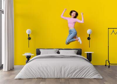 Full length photo of girlish adorable pretty woman dressed striped top jeans sneakers jumping hands up isolated on yellow color background Wall mural