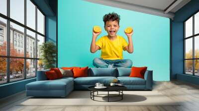 Full length photo of good mood small boy with brown hair wear stylish t-shirt sit hold sliced orange isolated on teal color background Wall mural