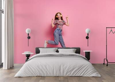 Full length photo of lovely teen lady jump run headphones listen music dressed stylish print clothes isolated on pink color background Wall mural