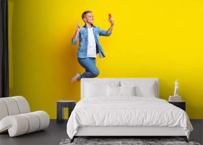 Full length photo of lovely young lady jumping selfie photo show v-sign dressed stylish denim garment isolated on yellow color background Wall mural